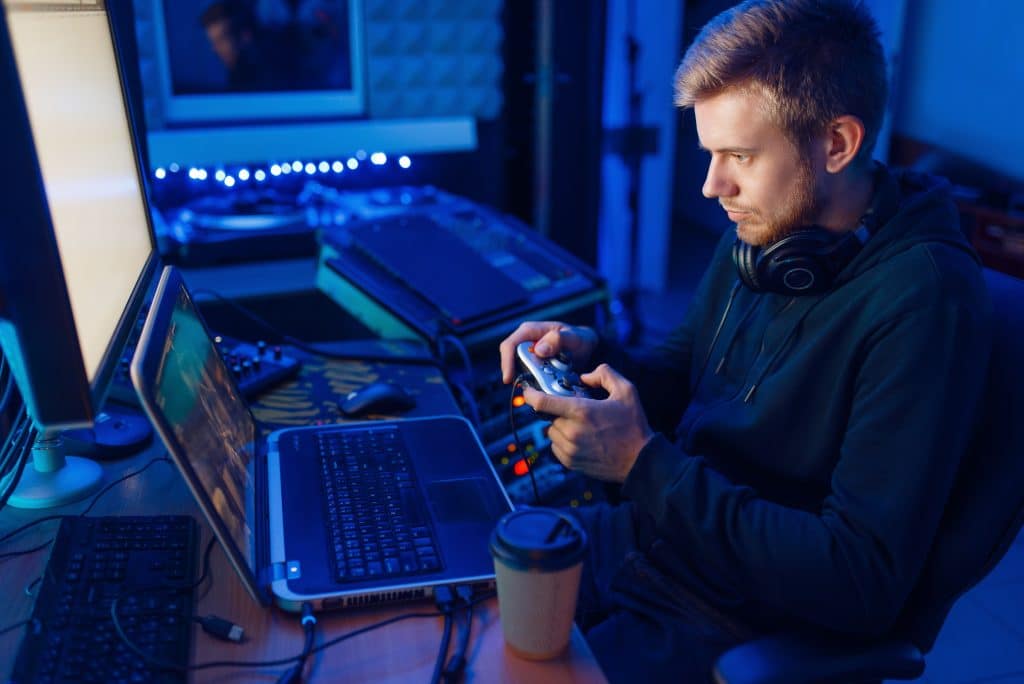 Male gamer in headphones holds joystick and playing videogame on console or desktop PC, gaming lifestyle, cybersport. Computer games player in his room with neon light, streamer
